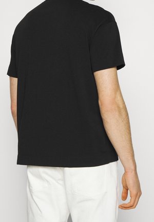 Musta lyhythihainen puuvillainen t-paita, jossa on rento istuvuus ja pyöreä pääntie, sileä pinta ja ei näkyviä logoja tai kuvioita.