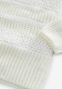 Pletena džemper u boji off-white s različitim teksturama, uključujući rebrovane i otvorene mrežaste dijelove, kratkim rukavima i horizontalnim prugama.
