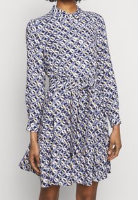 Blommig klänning med långa ärmar, knapp-ner krage, inzoomad midja, lager på lager volang i nyanser av blått, vitt och gult.