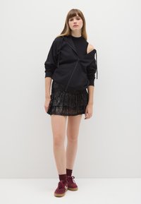 Felpa nera con zip e una spalla scoperta, abbinata a una mini gonna nera di paillettes con volant. Sneakers bordeaux con suole marroni.