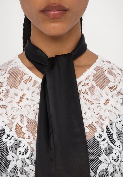 Black satin scarf tied at the neck, featuring smooth texture and elongated, flowing shape, worn over a white lace top with floral patterns.