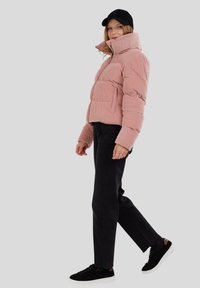 Różowa kurtka puchowa z szorsem o wysokim kołnierzu, z przednimi kieszeniami i zamkiem błyskawicznym. Noszona z czarnymi dżinsami i czarnymi trampkami.