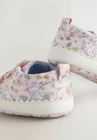 Scarpe in tessuto con motivo floreale in rosa pastello, con suola in gomma bianca. Presentano un rivestimento morbido e una piccola linguetta sul tallone per facilitarne l'indossamento.