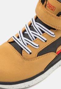 Sneaker in pelle color cuoio con accenti neri, lacci bianchi e una fascia in velcro. Presenta una superficie testurizzata e una suola bianca decorata.