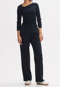 Mörkblå ribbad tröja med asymmetrisk halsringning, ihopparad med mörka byxor med dragsko i midjan och sidofickor. Vita avslappnade skor.