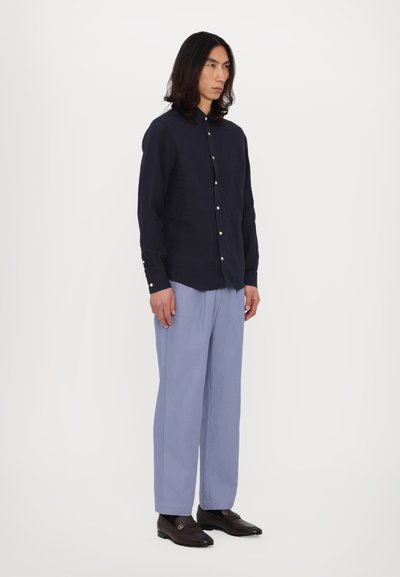 Cămașă din in bleumarin cu nasturi, pantaloni largi de un albastru deschis, loafers maro cu accente de aur, textură fină, croială lejeră.