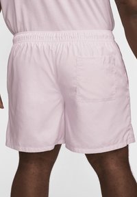 Shorts de bain rose clair avec une taille élastique, tissu léger et une poche arrière. Texture lisse avec un design simple.