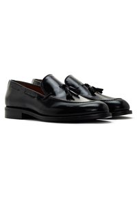 Mocassins en cuir noir avec une finition brillante, ornés de pampilles et de coutures raffinées. Talon bas et carré pour un soutien stable.