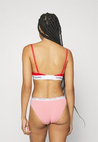 Des bretelles rouges réglables et une bande blanche avec "TOMMY JEANS" sur un soutien-gorge associé à des culottes en coton rose clair, avec une taille blanche.
