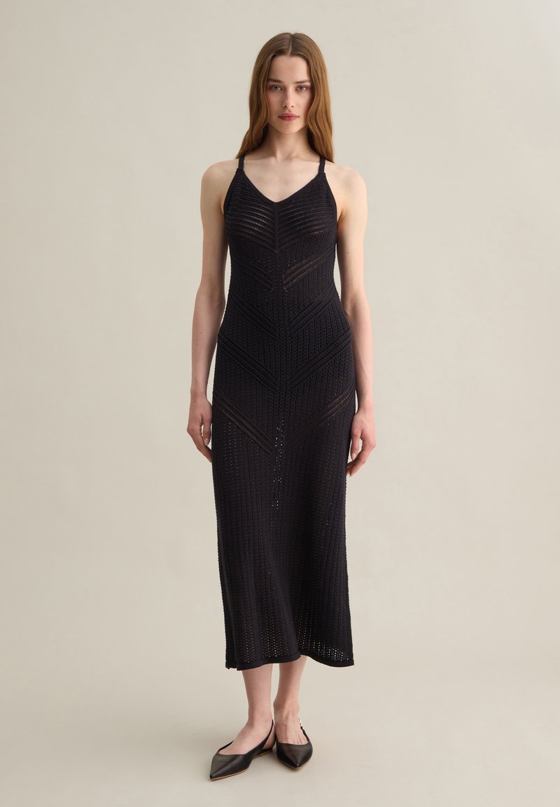 Abito midi nero in maglia con scollo a V, spalline sottili e motivi geometrici. Presenta un corpetto aderente e un orlo svasato. Abbinato a ballerine con punta.