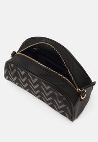 Sac en nylon noir avec une fermeture éclair dorée. Présente un motif chevron gris sur le devant et une texture lisse. Inclus une poignée sur le dessus.