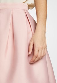 Falda plisada de color rosa claro con una textura suave y una cinturilla ajustada, que presenta profundos pliegues de cuchillo que generan volumen alrededor del dobladillo.