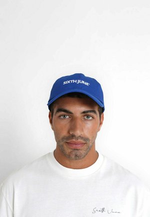 Blauwe pet met het logo "SIXTH JUNE" in het wit, gestructureerd ontwerp, gebogen klep, gecombineerd met een lichtgekleurde, ronde hals sweatshirt.