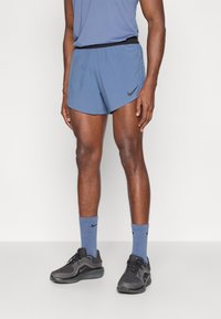 Ανδρικές αθλητικές κοντές φόρμες Nike σε ανοιχτό μπλε χρώμα, με μαύρη ελαστική μέση και λογότυπο. Συνδυάζονται με μπλε κάλτσες και μαύρα αθλητικά παπούτσια.