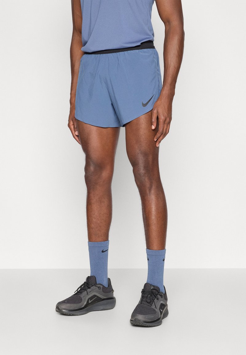 Ανδρικές αθλητικές κοντές φόρμες Nike σε ανοιχτό μπλε χρώμα, με μαύρη ελαστική μέση και λογότυπο. Συνδυάζονται με μπλε κάλτσες και μαύρα αθλητικά παπούτσια.