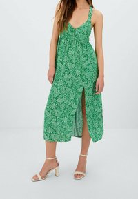 Vihreä maksimekko, jossa on paisley-kuvio, V-pääntie, säädettävät olkaimet, sivureikä ja kevyt kangas. Yhdistettynä vaaleanruskeisiin remmi-korkokenkiin.