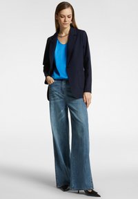 Marineblå kavaj över en blå topp, vida denimjeans med blekt tvätt, och svarta spetsiga skor. Enkelt halslinje med accessoarer.