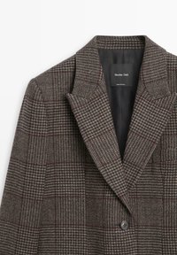 Blazer a quadri marrone realizzato in tessuto testurizzato; presenta un colletto a revers e una chiusura con un singolo bottone nero. Etichetta interna visibile.