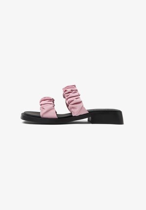 Pink fabric sandals with ruched upper bands and a black, chunky sole. Smooth texture, open design, and flat heel for casual wear.
