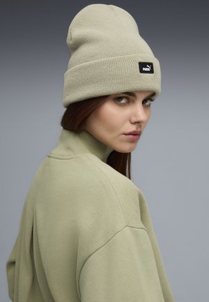 Lys grøn strikket hue med et sort Puma-logo patch, båret med en matchende lys grøn sweatshirt med høj hals. Glat tekstur, afslappet pasform.
