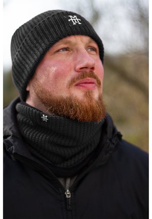 Black ribbed knit beanie and scarf set, featuring a subtle logo, worn over a dark jacket. The fabric appears warm and textured.