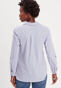 Chemise à manches longues de couleur bleu clair et motif blanc avec des accents rouges, dotée d'un col, de poignets à boutons et de détails de pli au dos.