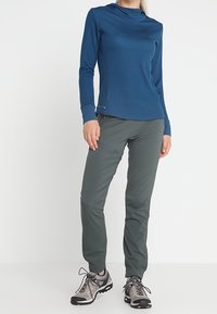 Blå långärmad topp, grå byxor och svarta vandringsskor. Toppen har en hög halsringning och en slät textur; byxorna är avsmalnande och i ett lätt material.