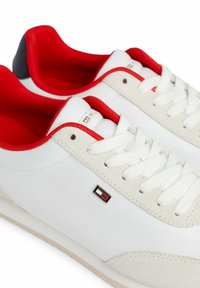 Białe sneakersy z gładką skórzaną cholewką, z czerwonymi akcentami i zamszowym wykończeniem. Posiadają sznurowane zapięcie i szczegół z logo marki.
