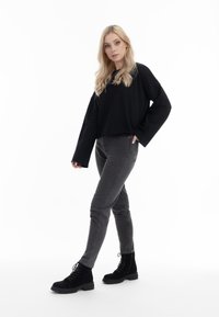Tricou negru cu mânecă lungă, asociat cu blugi gri și cizme negre cu șireturi până la gleznă. Ținuta are un croi lejer și o textură de țesătură moale.