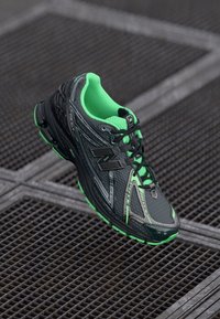 Chaussure de sport noire et verte avec une tige en maille, des accents synthétiques et une semelle texturée. Caractéristiques : détails réfléchissants et fermeture à lacets.