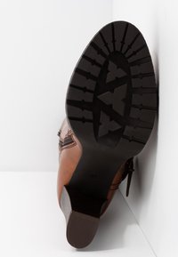 Bottine en cuir marron avec une semelle en caoutchouc texturée, présentant une couture diagonale et un talon courbé. La semelle affiche un motif de bande de roulement prononcé.