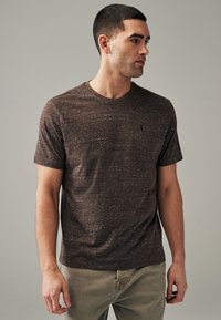 T-shirt marrone a maniche corte con finitura testurizzata, scollatura tonda e design minimalista, caratterizzato da un piccolo logo sul petto.