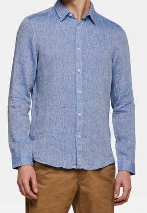 Hellblaues Hemd mit Knöpfen aus strukturiertem Stoff, mit Kragen, langen Ärmeln und weißen Knöpfen, kombiniert mit khakifarbenen Hosen.