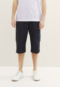 Navy Cargo-Shorts aus leichtem Stoff mit zwei Seitentaschen, regulärer Passform und knielangem Design, kombiniert mit weißen Sneakers.
