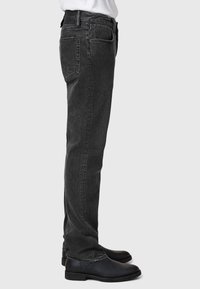 Mustat farkut suoranlahkeisella leikkauksella, joissa on takataskut ja hienovarainen kuluminen. Yhdistetty mustien nahkakenkien kanssa.