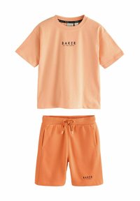 Conjunto de camiseta y pantalones cortos de algodón color melocotón con cuello redondo, estampado de logo en la parte delantera, cintura elástica y cordón. Textura suave.