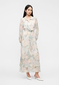 Μακρύ, αέρινο φόρεμα από ελαφρύ ύφασμα με απαλά, παστέλ ανθικά σχέδια. Διαθέτει γιακά, μακριά μανίκια και ζώνη που δένει στη μέση.