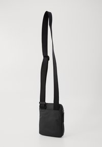 Sac bandoulière noir avec un extérieur en tissu lisse, de forme rectangulaire, une sangle réglable et une fermeture zippée. Design minimaliste avec des lignes épurées.