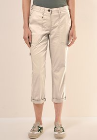 Beige, cropped broeken met zijzakken, opgerolde manchetten en een gladde textuur. Gecombineerd met sneakers met groene accenten.