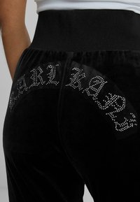 Mustad sametist joggersitest, millel on kõrge vöökoht ja rhinestone'idega kaunistatud "KARL" tekst taga. Sile tekstuur ja keha lähedane lõige.