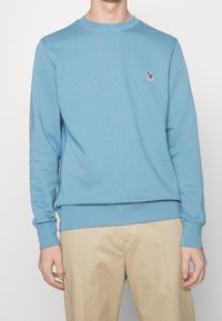 Felpa in cotone azzurro chiaro con collo a girocollo, polsini e orlo a coste. Presenta un piccolo design ricamato sul lato sinistro del petto.