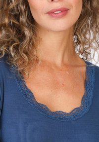 Blaues geripptes Oberteil mit einem gewellten Spitzen-Ausschnitt, das eine glatte Textur und ein figurnahes Design präsentiert, mit einem Nahaufnahme-Ansicht des Stoffdetails.