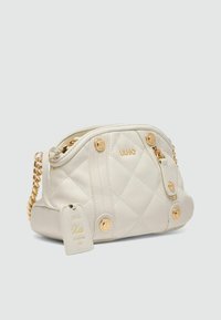 Cremefarbenes, gequiltetes Handtasche mit goldenen Hardware-Elementen, Kettenriemen und Logo-Akzenten. Verfügt über einen seitlichen Reißverschluss, dekorative Knöpfe und ein Etikett mit der Aufschrift "Kate".