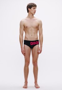 Črne plavalne športne hlače z teksturiranim vzorcem in izrazitim roza logotipom "DSQUARED2" na pasu, ki jih nosi moški model.