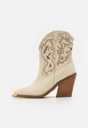 Bottine style western en cuir crème avec motifs découpés détaillés et talon bloc empilé en bois.