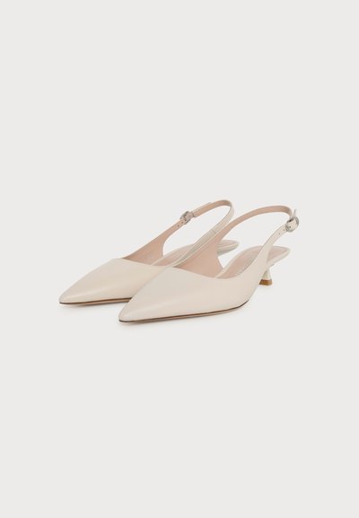 Paire d’escarpins slingback beiges à bout pointu avec petit talon kitten et fines brides à la cheville, présentée sur un fond blanc uni.