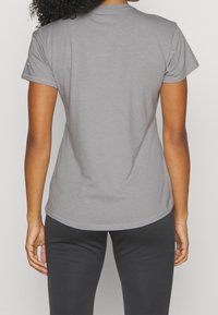 Grå kortärmad t-shirt med rundad nederkant och mjuk textur. Har en rund halsringning och avslappnad passform, kombinerad med svarta leggings.