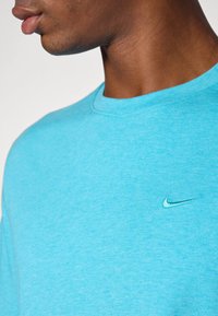 Türkiissinine Nike t-särk, lühikeste varrukatega, ümmarguse kaelusega, pehme tekstuuriga, millel on rinna peal väike roheline logo.