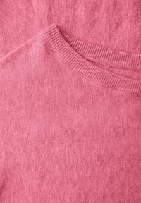 Dettaglio di un maglione rosa con una texture liscia, scollatura a coste e un sottile motivo sfumato. Materiale morbido dall'aspetto accogliente.