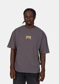 Šedé oversized tričko s kulatým výstřihem, se malým žlutým logem uprostřed. Vyrobeno z měkkého bavlněného materiálu.
